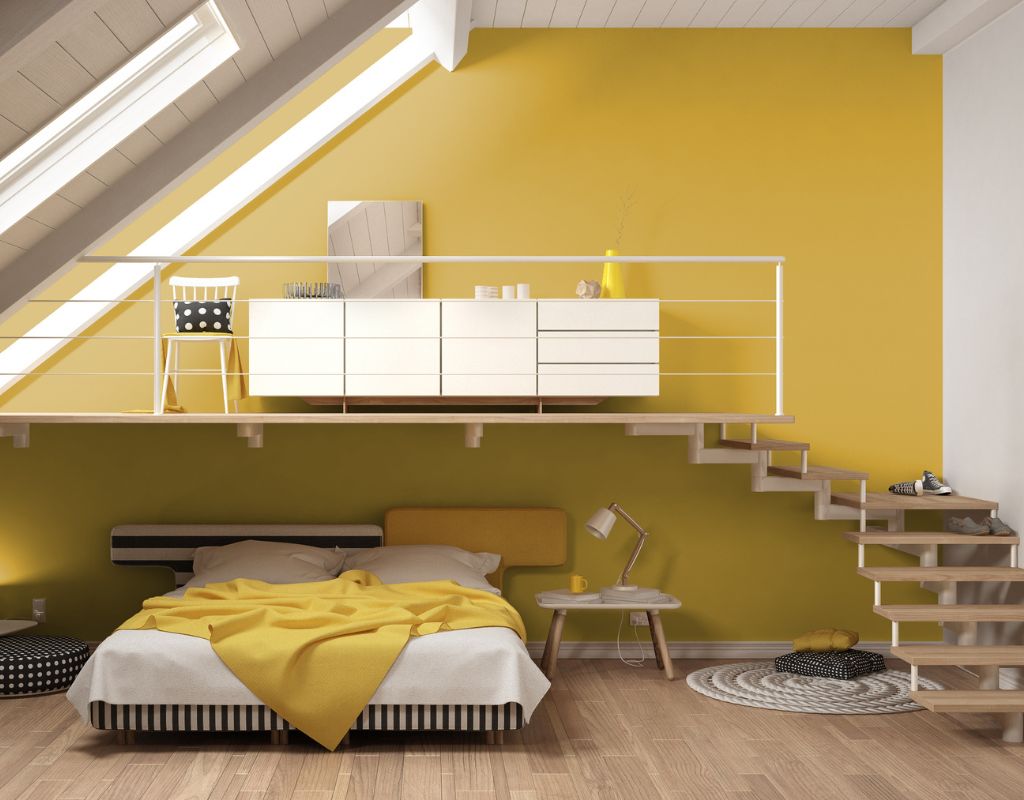 Mansarda ristrutturata con pareti gialle, letto moderno e zona studio sopraelevata con scala di legno