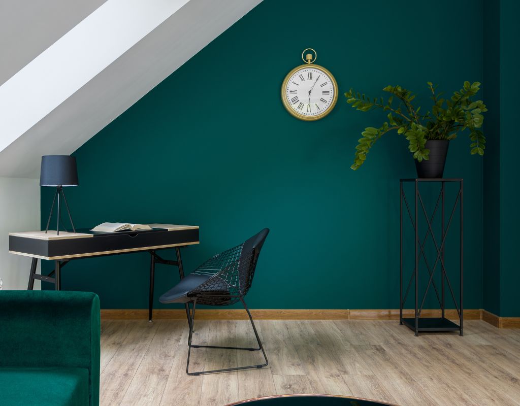 Questo studio modernamente ristrutturato a Milano sfoggia una parete verde accattivante, complementata da un elegante tavolo da lavoro nero, una sedia dal design unico, e dettagli come una lampada da tavolo blu e un orologio vintage. L'arredamento è stato scelto per ottimizzare lo spazio sotto una mansarda inclinata, dando un tocco di classe e funzionalità all'ambiente.